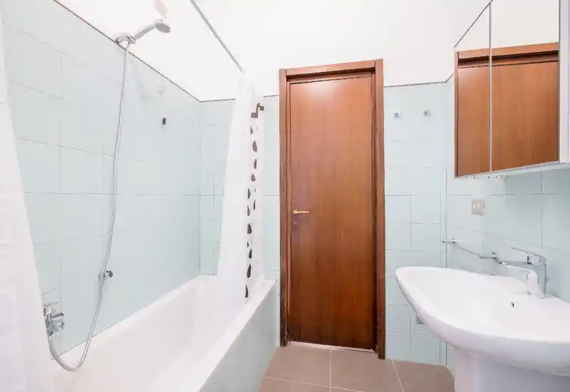 Bagno luminoso e pulito con vasca e doccia, lavabo bianco e piastrelle azzurre; ambiente semplice e ben illuminato ideale per annunci.