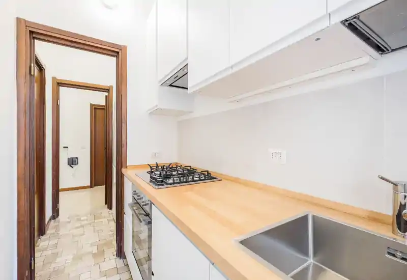 Cucina compatta moderna e luminosa con piano di lavoro in legno, fuochi a gas incassati e lavello in acciaio inox — pratica per un appartamento.