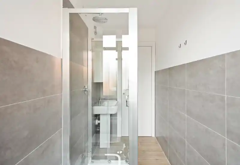 Bright, modern bathroom with a glass shower cabin, wall-mounted sink and large grey tiles creating a clean, minimal look.