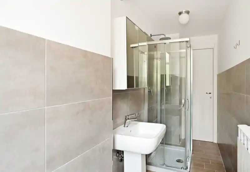 Modern, compact bathroom with glass shower enclosure, pedestal sink and mirrored cabinet; neutral tiles and bright lighting create a clean, contemporary feel.