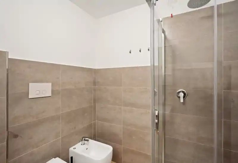 Baño moderno y compacto con paredes alicatadas, plato de ducha y bidé; tonos neutros y grifería limpia para un aspecto minimalista.