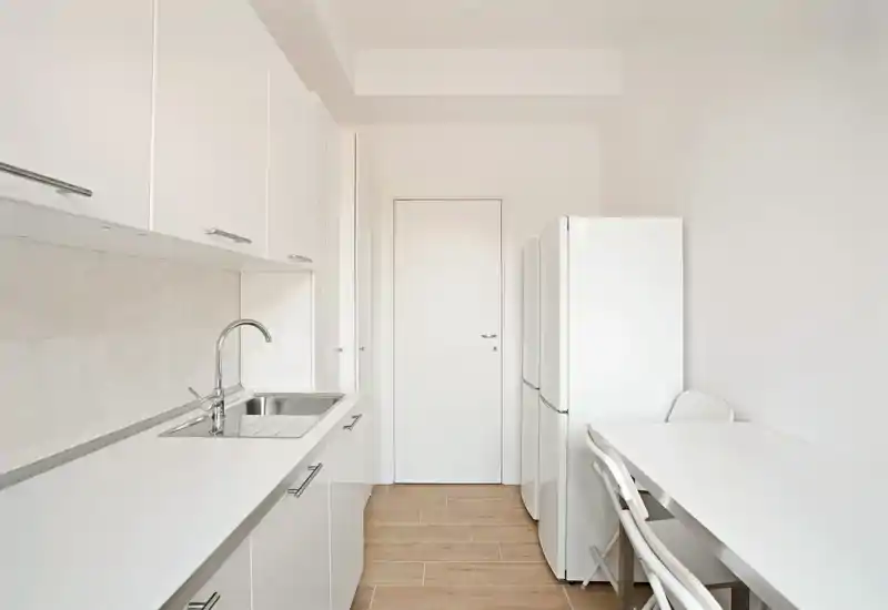 Cucina a corridoio luminosa e moderna con mobili bianchi, lavello integrato e piccolo piano pranzo — design minimale ideale per appartamenti piccoli.