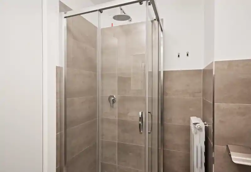 Ducha moderna con mampara de vidrio, cabezal de ducha techo y azulejos en tonos neutros; luminoso, limpio y funcional.