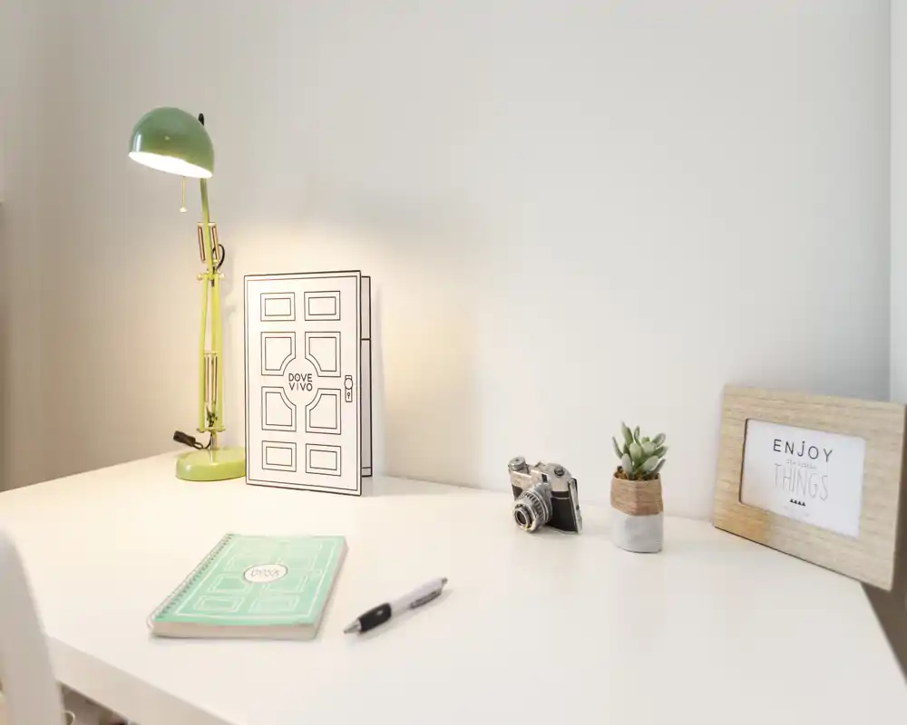 Angolo scrivania luminoso e minimal con una lampada verde, cornice decorativa, piccola pianta e macchina fotografica vintage — un angolo lavoro accogliente e ben illuminato.