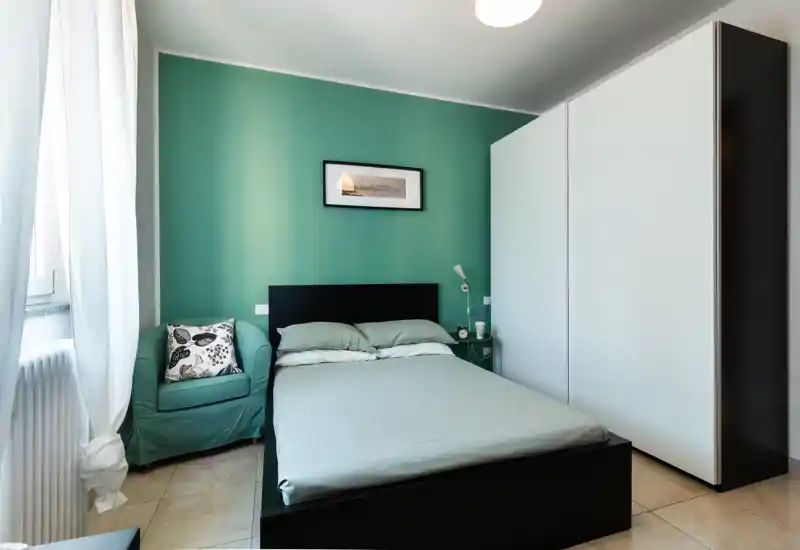 Dormitorio luminoso y bien decorado con cama doble, cojines a juego y un sillón acogedor junto a la ventana. Un gran armario y una decoración minimalista crean un ambiente moderno y tranquilo, ideal para alquileres vacacionales.