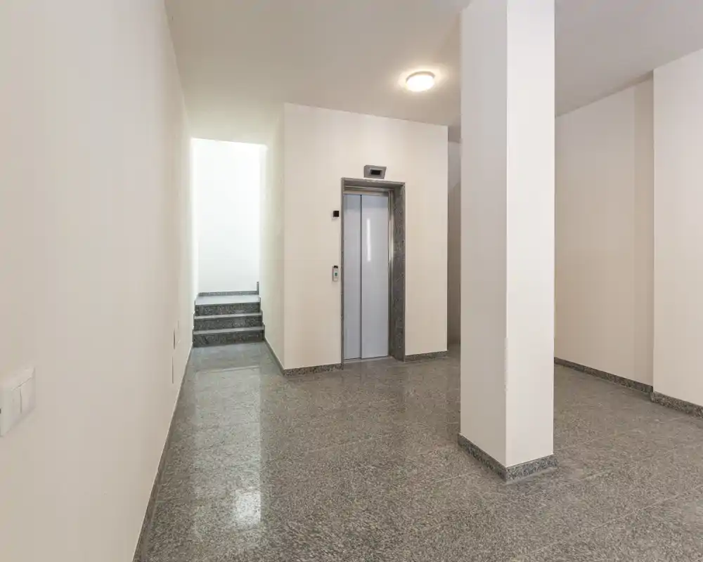 Ingresso condominiale moderno e pulito con ascensore, pavimento in pietra lucida e pareti neutre — area comune luminosa e minimalista.