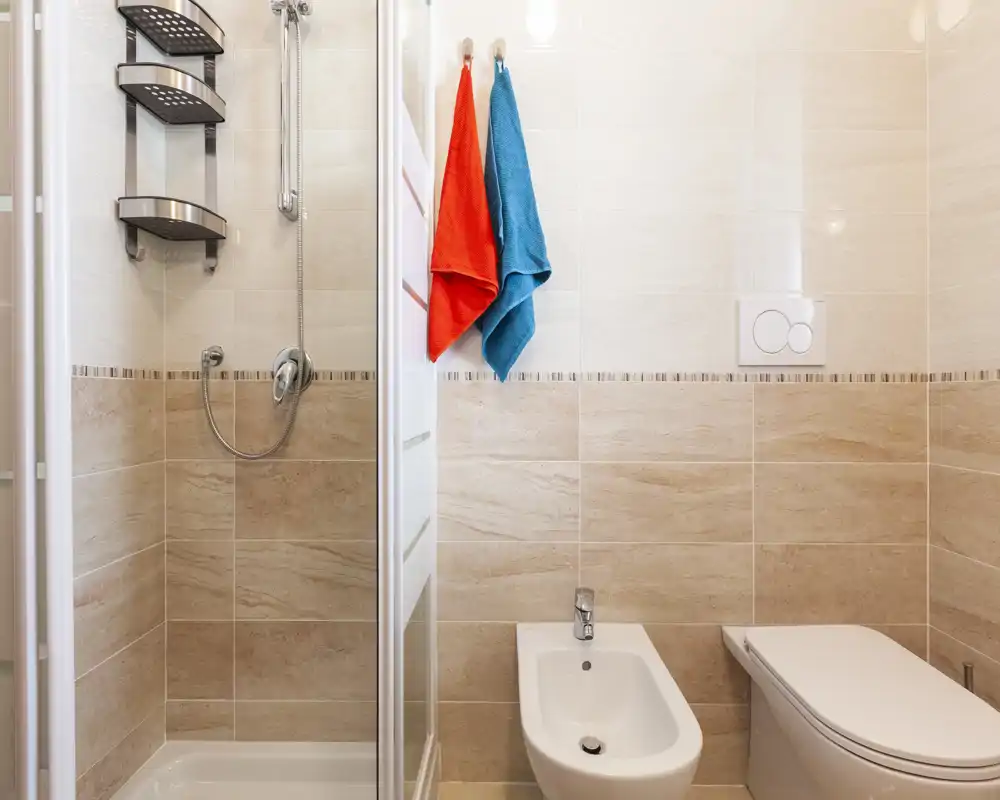 Bagno moderno e pulito con cabina doccia, bidet e WC; piastrelle beige neutre e asciugamani colorati per un tocco fresco.