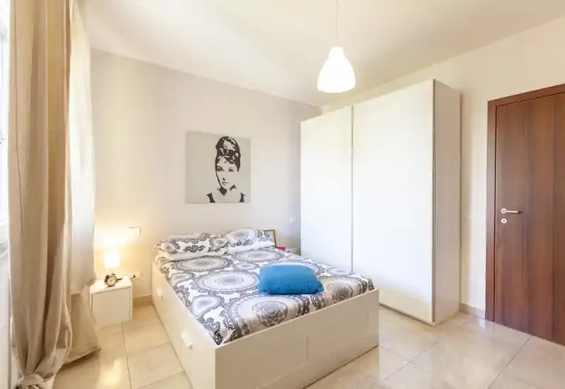 Camera da letto luminosa e ben allestita con letto matrimoniale, biancheria a fantasia e grande armadio bianco; toni neutri e luce naturale per un'atmosfera moderna e rilassante.
