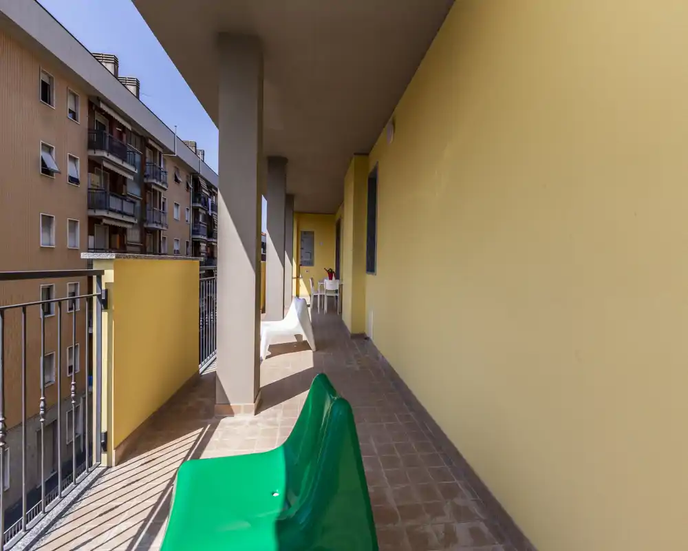 Balcone soleggiato arredato con sedute e pavimento piastrellato, affacciato sui palazzi vicini: area esterna luminosa e spaziosa ideale per rilassarsi.