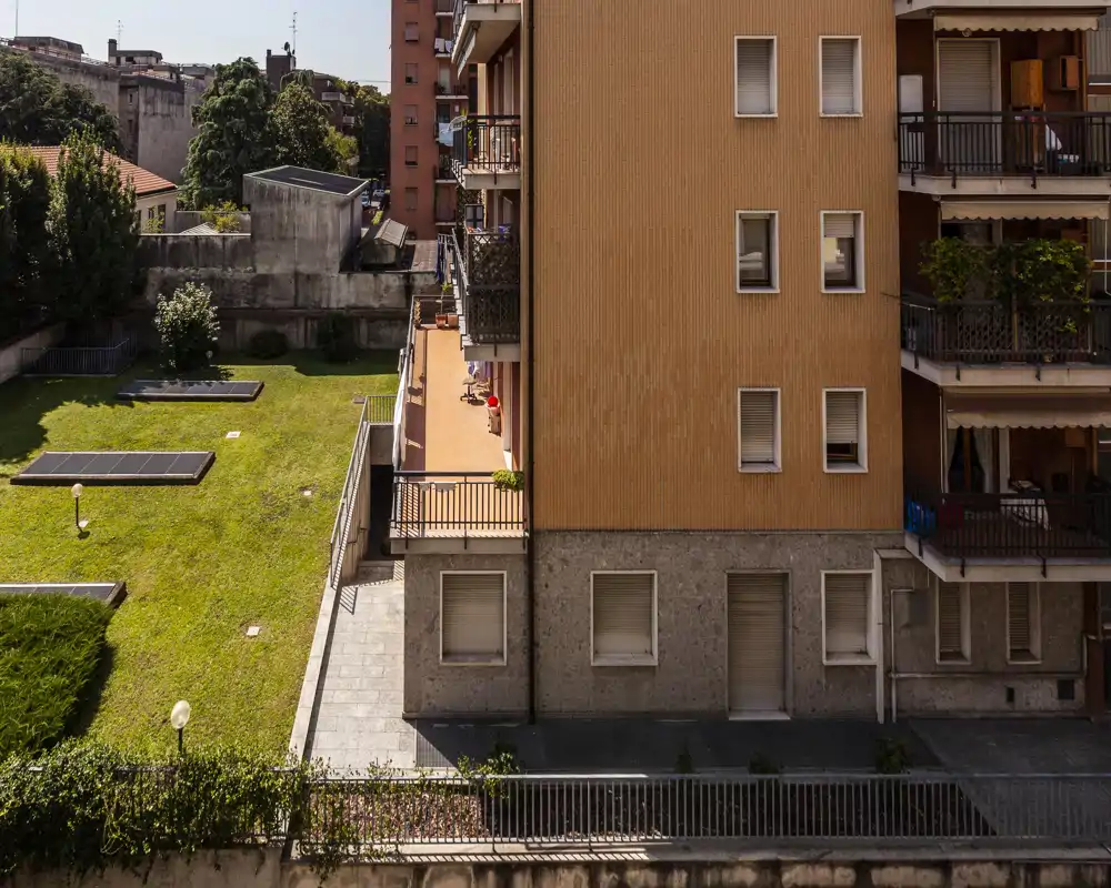 Vista esterna di un condominio con cortile erboso, terrazze e balconi, fotografato alla luce del giorno.