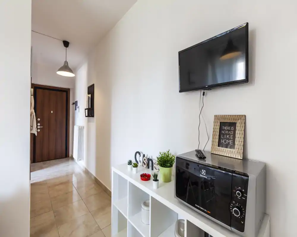 Ingresso luminoso e ordinato con mensola decorativa, TV a parete e porta d'ingresso visibile — allestimento curato ideale per un annuncio.