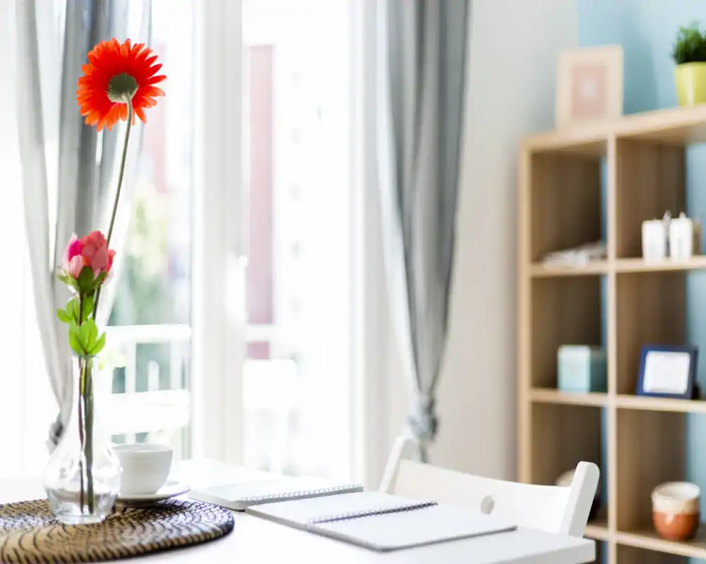 Bright, styled dining corner with a small table, decorative vase and natural light through large windows — ideal for morning coffee or light meals.