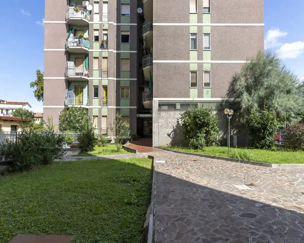 Sunny courtyard with paved walkway and grassy lawn in front of a residential building; ideal for describing outdoor communal space.