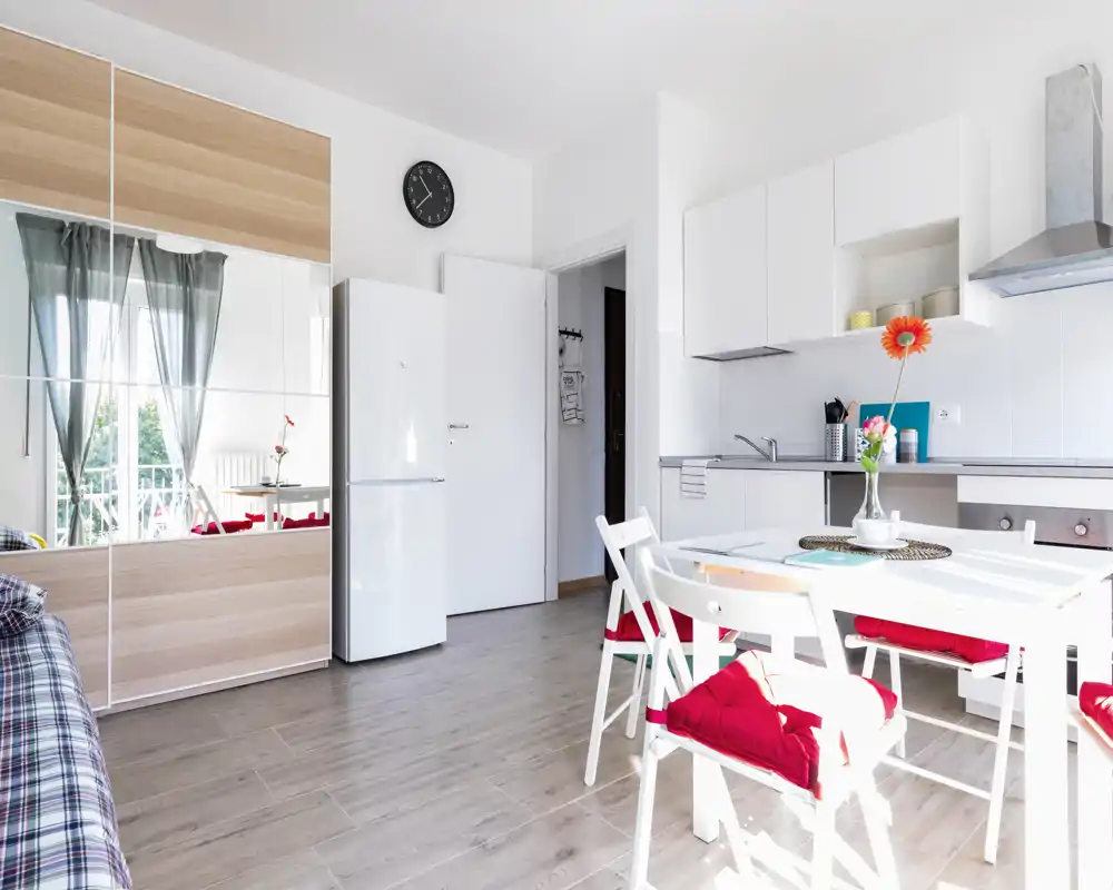 Bright open kitchen area with modern white cabinets, a dining table with red-cushioned chairs and tasteful decorative accents; ideal for rental listings highlighting light and clean design.