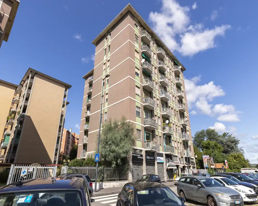 Exterior view of a multi-storey residential building with balconies and street parking, captured in bright daylight.