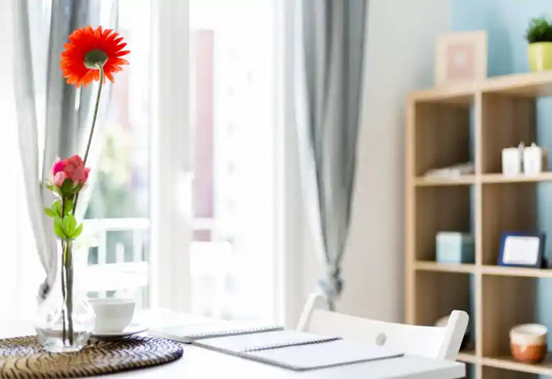 Angolo pranzo luminoso e curato con un piccolo tavolo, vaso decorativo e luce naturale da ampie finestre — perfetto per colazioni o pasti leggeri.