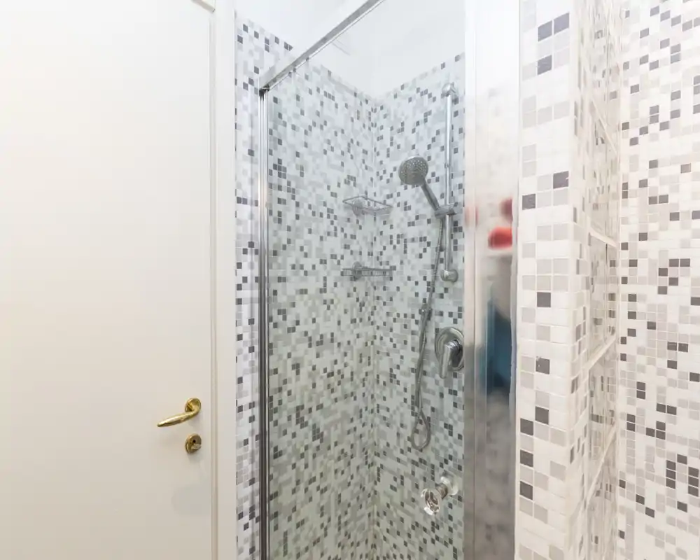 Bagno moderno con box doccia in vetro, rivestimento a mosaico e doccia a mano; ambiente pulito, luminoso e curato.