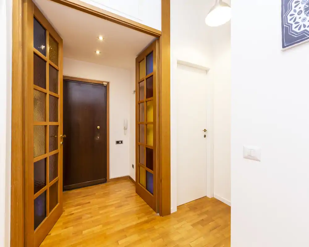 Ingresso luminoso con pavimento in legno e porta d'ingresso solida; porte a doppia anta con vetri decorativi donano carattere.
