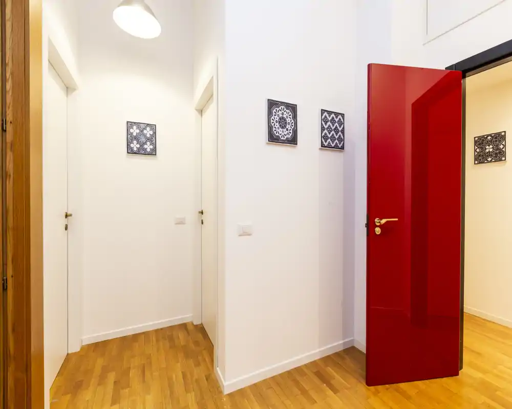 Ingresso/corridoio moderno e luminoso con pavimento in legno caldo, pareti bianche pulite e una porta rossa vivace; piastrelle decorative a parete aggiungono stile.