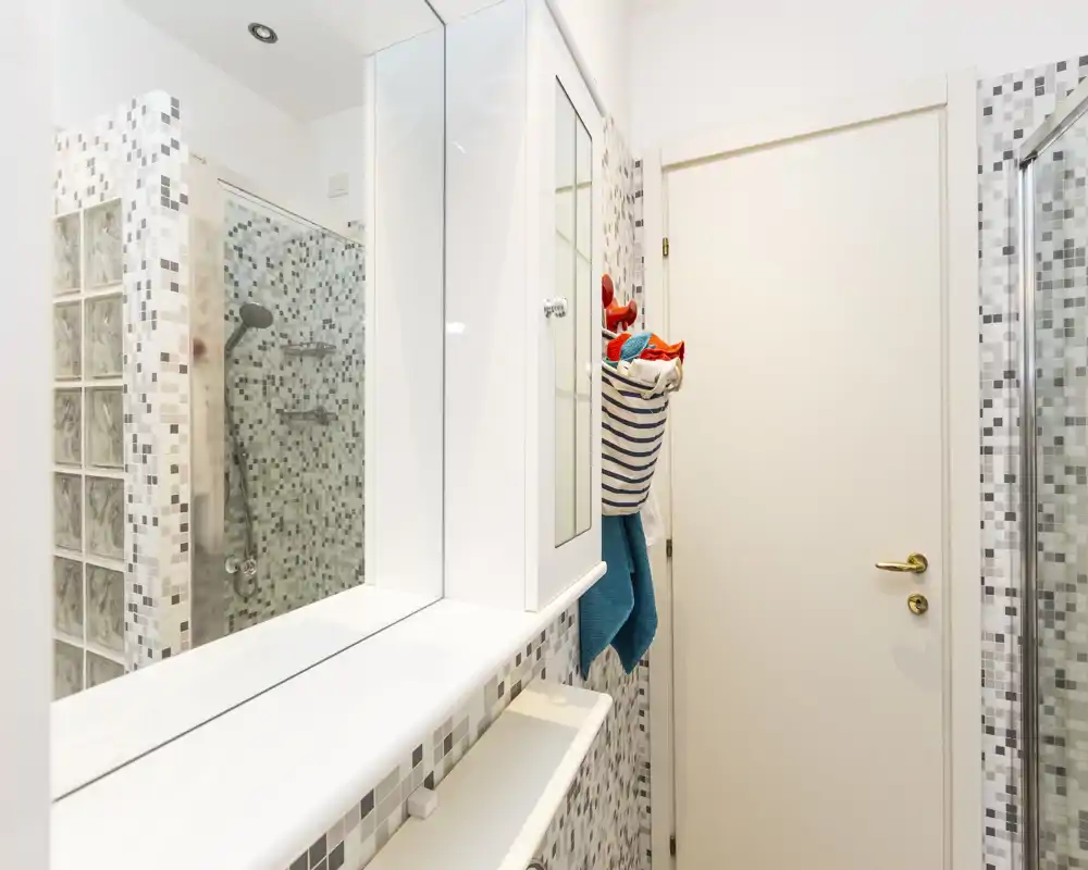 Bagno moderno compatto con box doccia in vetro, piastrelle a mosaico e mobile a parete. Spazio luminoso e pulito con accessori contemporanei e vani per riporre.