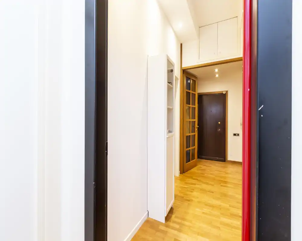 Ingresso luminoso e stretto con pavimento in parquet, una nicchia contenitiva e la porta d'ingresso visibile in fondo. Spazio d'ingresso pulito e moderno, adatto per un annuncio di affitto.