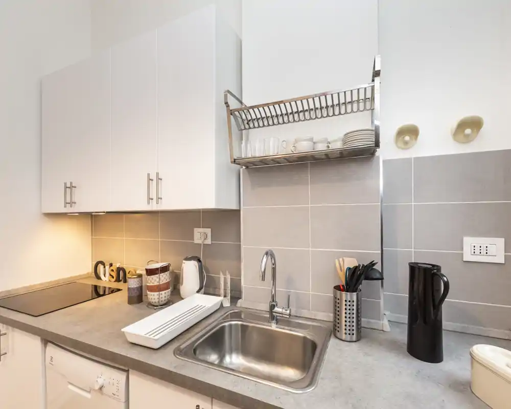 Cucina moderna compatta con lavello in acciaio, piano a induzione, pensili e accessori ordinati sul piano — ambiente luminoso, pulito e funzionale.