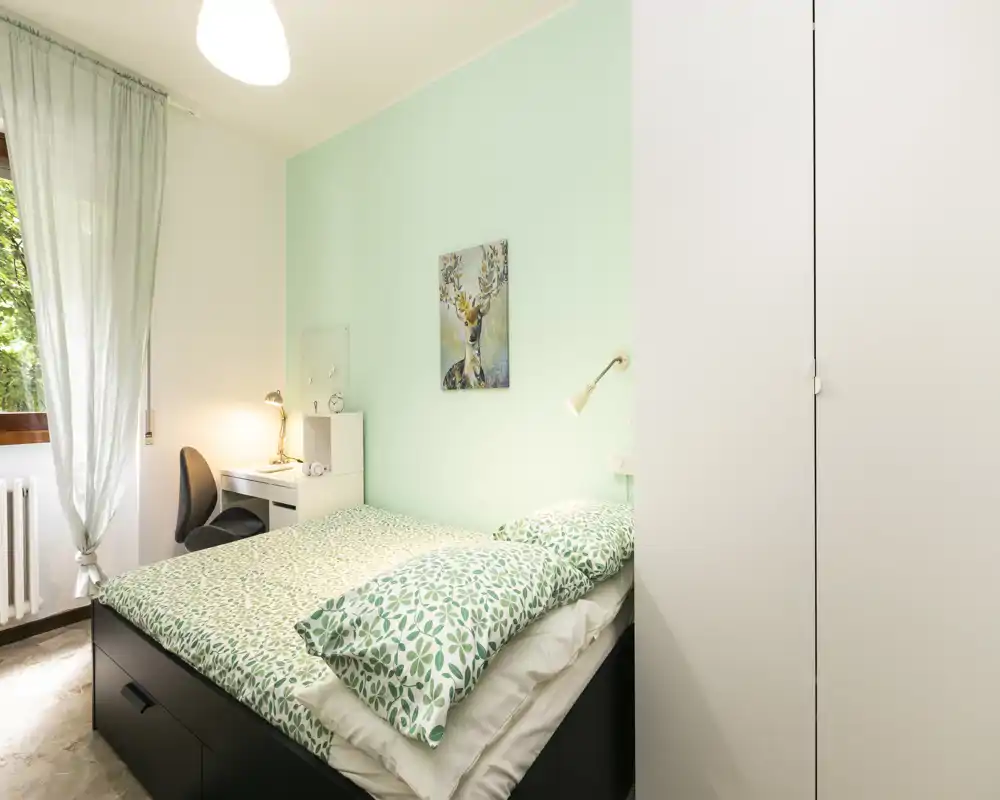 Dormitorio luminoso y cuidado con cama doble con ropa de cama verde estampada, pequeño escritorio junto a la ventana y armario empotrado: perfecto para una estancia cómoda para una o dos personas.