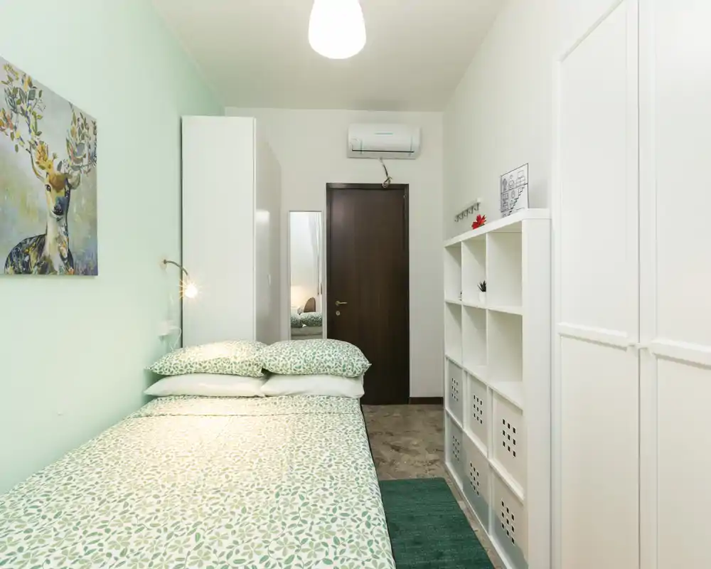 Dormitorio bien presentado y luminoso con cama doble con ropa de cama verde estampada, armarios blancos y luz ambiental suave — perfecto para alquileres vacacionales.