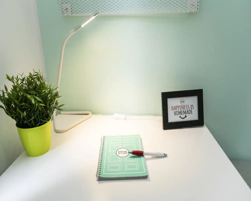 Angolo scrivania luminoso e ordinato con agenda, penna, lampada da tavolo e una piccola pianta in vaso — ideale per lavorare o studiare in uno spazio minimal e tranquillo.
