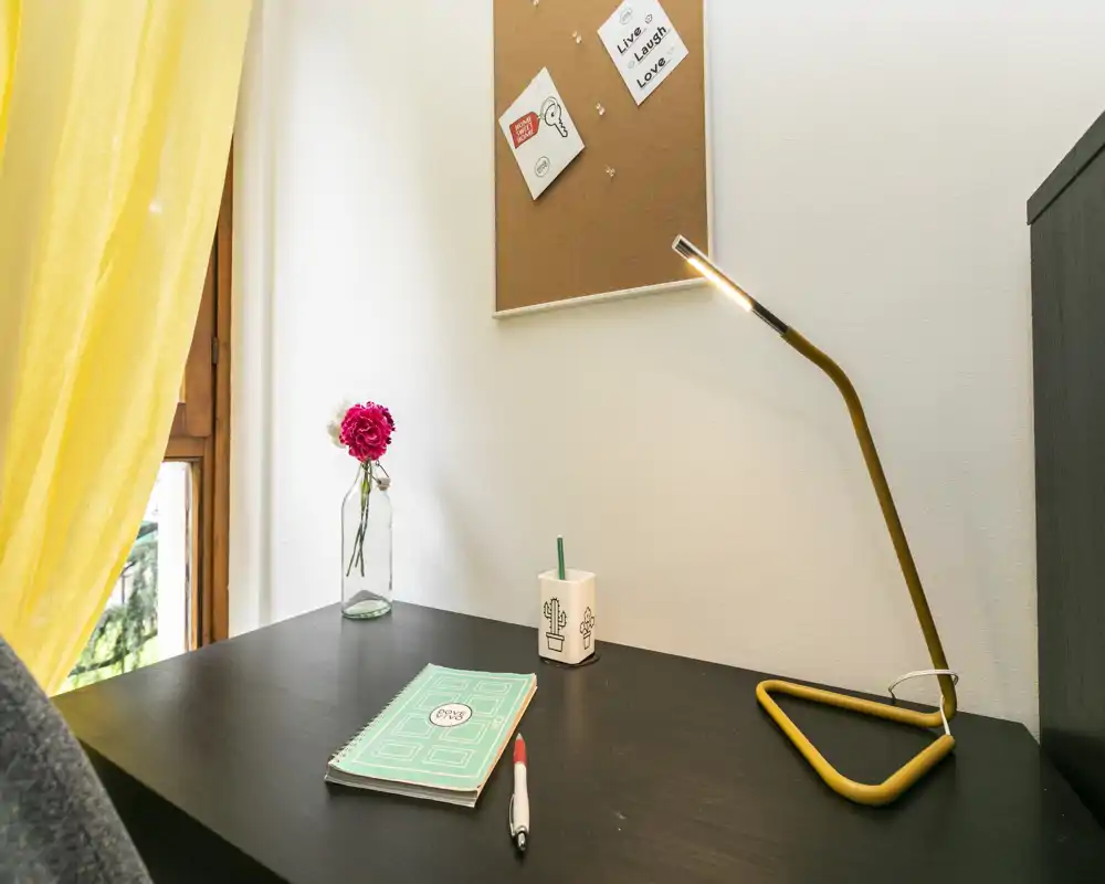 Angolo scrivania luminoso e ordinato con una lampada gialla moderna, un quaderno e un piccolo vaso — un accogliente spazio di lavoro vicino alla finestra.