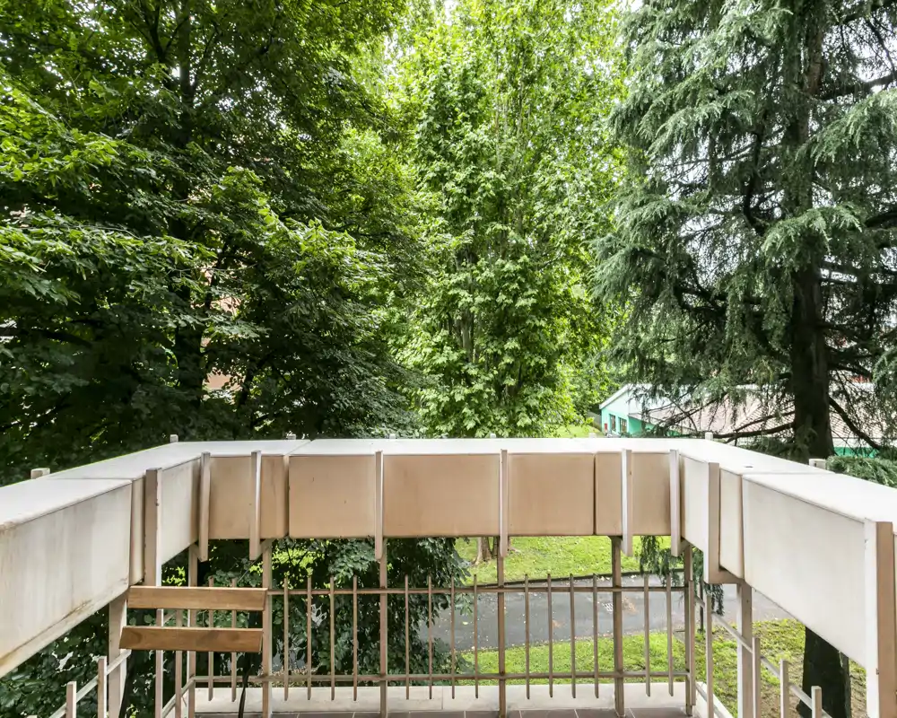 Balcone soleggiato con vista su alberi maturi e una strada tranquilla — ideale per colazione e momenti di relax all'aperto.