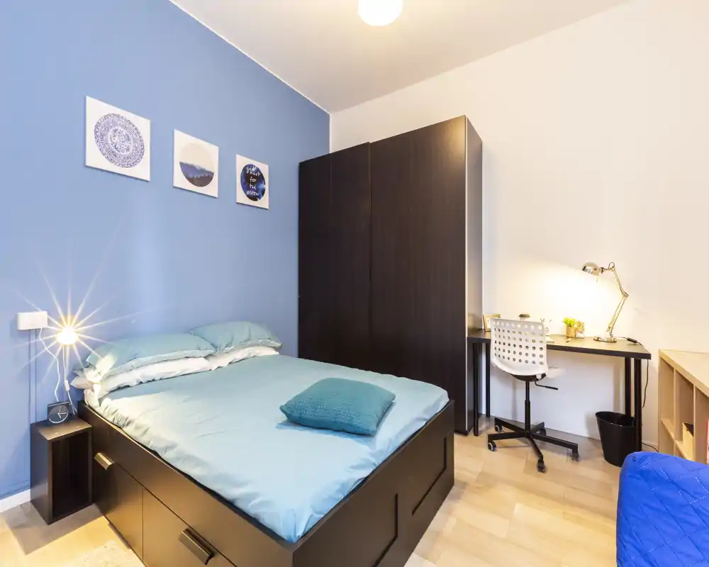 Camera da letto moderna e luminosa con letto matrimoniale, biancheria turchese coordinata, un ampio armadio e una scrivania con lampada, ideale per lavoro o studio.
