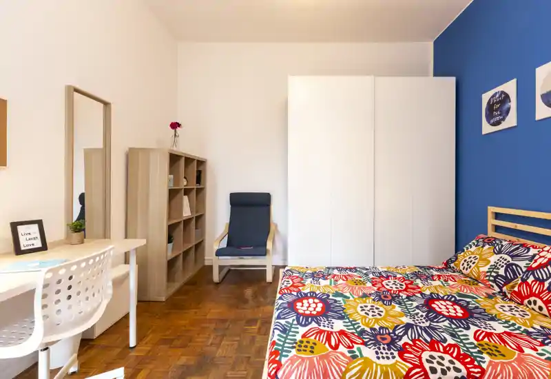 Bright, well-styled bedroom with a colorful bedspread, white wardrobe and a desk area — ideal for a single renter or student.