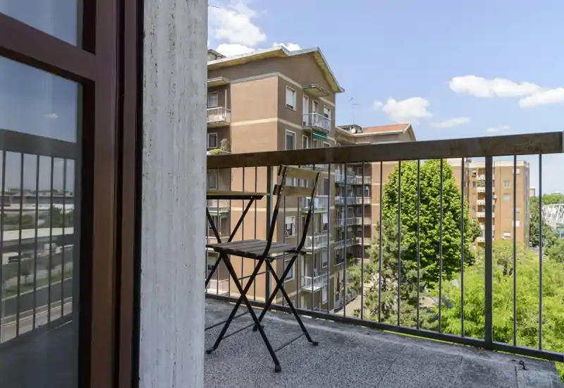 Sunny balcony with a small bistro table and chair, overlooking neighboring apartment buildings and treetops — ideal for morning coffee.