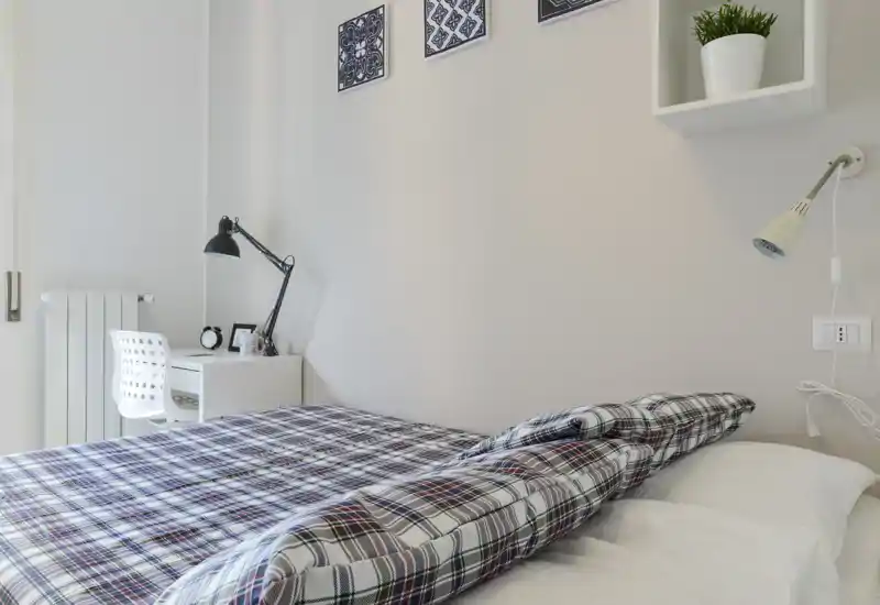 Bright, modern bedroom with a patterned duvet, bedside lamp and a small desk area—clean, uncluttered and well lit, ideal for rental listings.