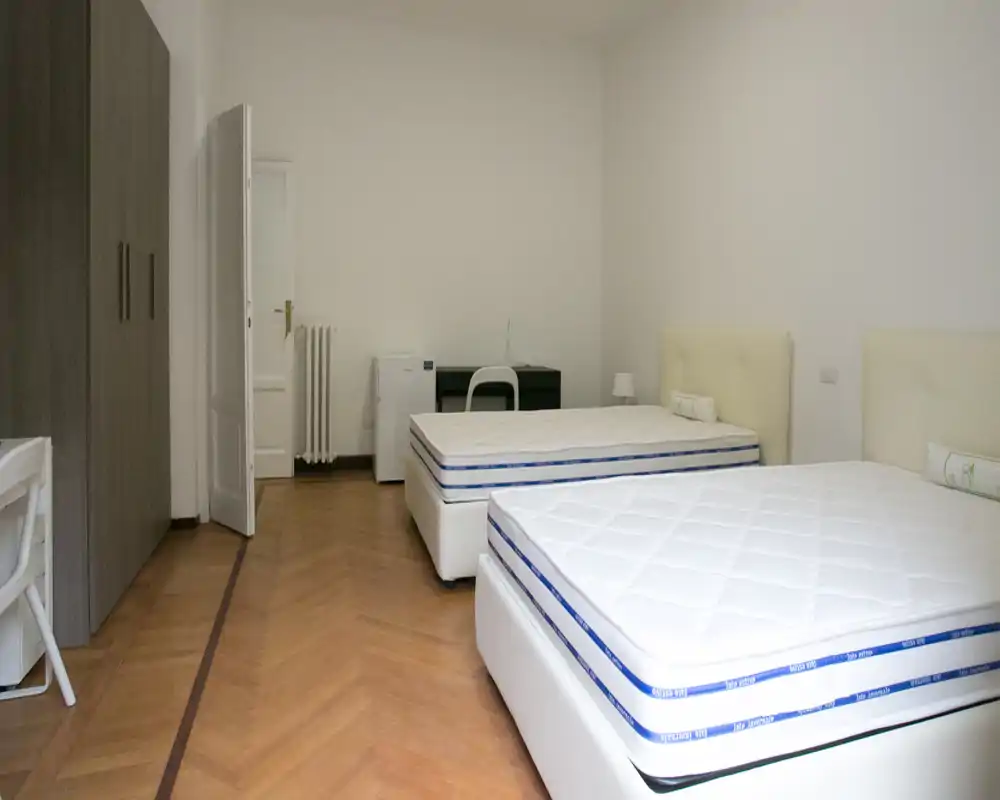 Dormitorio amplio y sencillo con dos camas individuales, cabeceros claros, suelo de parquet y armario empotrado — luminoso y despejado, ideal para ocupación doble.