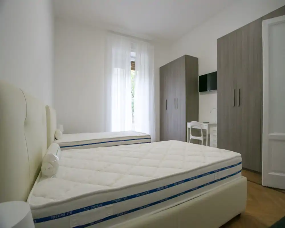 Dormitorio luminoso y minimalista con dos camas individuales, tonos neutros y amplios armarios — ideal para estancias compartidas.