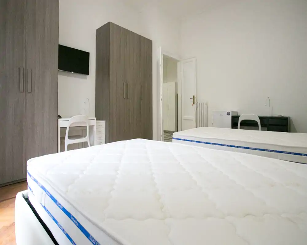Dormitorio luminoso con dos colchones individuales, armarios modernos y escritorios sencillos — limpio, minimalista y bien iluminado, ideal para alquileres temporales.
