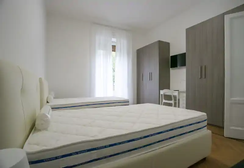 Camera da letto luminosa e minimal con due letti singoli, toni neutri e ampi armadi — ideale per soggiorni condivisi.