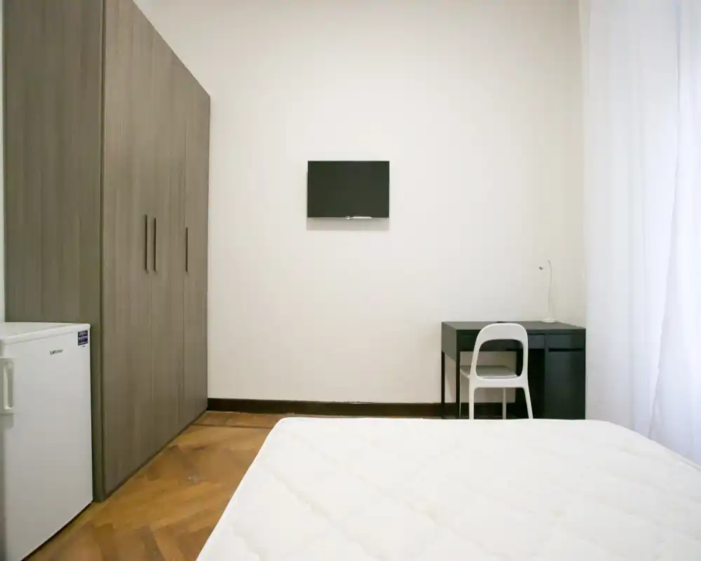 Dormitorio luminoso y minimalista con colchón en primer plano, amplio armario, pequeño escritorio y TV en la pared: sencillo, limpio y bien iluminado para el anuncio.