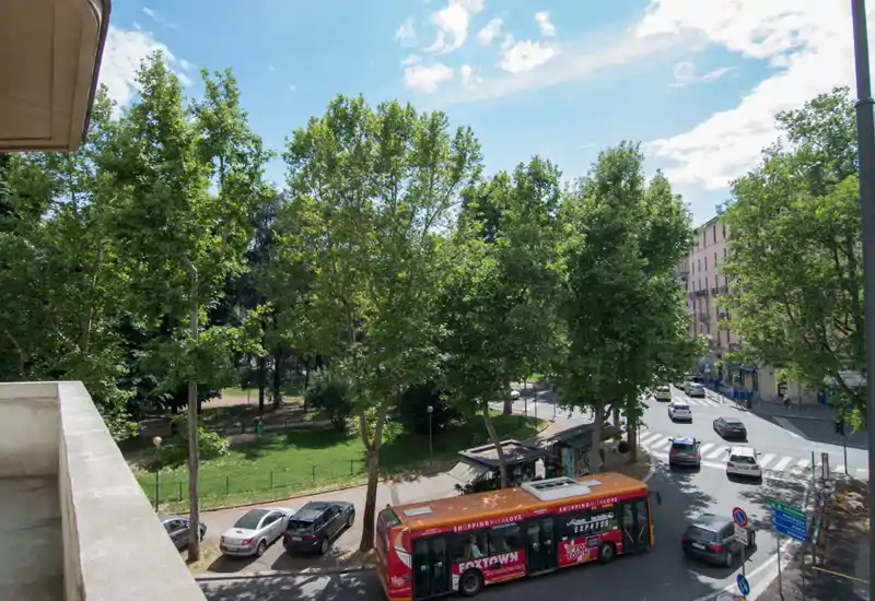 Vista soleggiata dalla balconata su una strada con alberi, un parco e una fermata dell'autobus: perfetta per mettere in evidenza la posizione e i trasporti vicini.