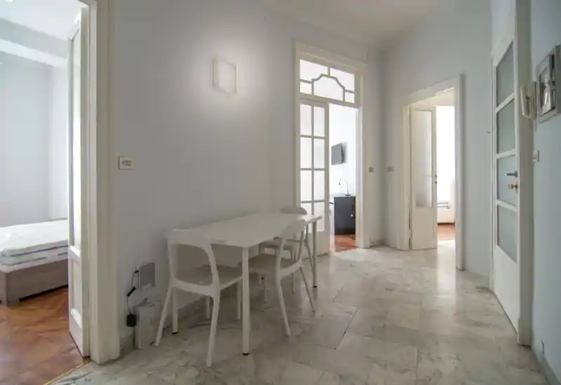 Piccolo angolo pranzo in un appartamento luminoso e minimalista con tavolo e sedie bianchi posizionati vicino alle porte che collegano le camere.