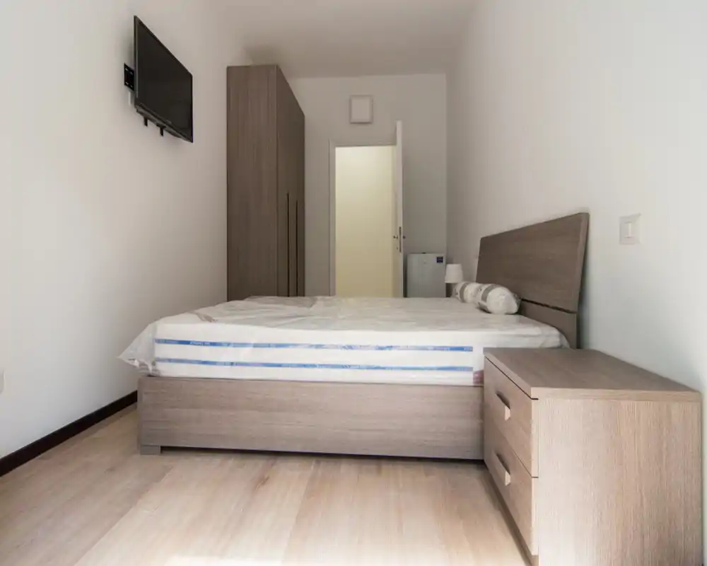 Dormitorio moderno y luminoso con cama doble, cabecero y mesita a juego y armario; tonos neutros y decoración sencilla que crean un espacio funcional ideal para alquileres temporales.