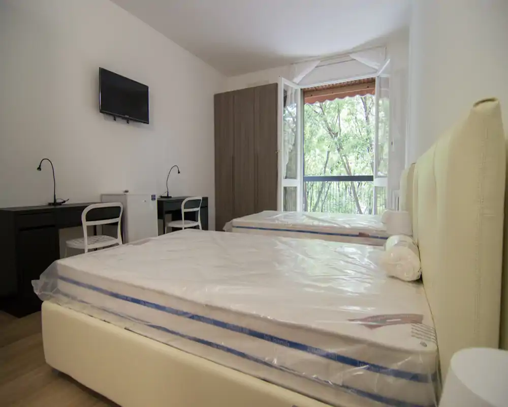 Bright twin-bedroom with two new mattresses, a large wardrobe and a balcony overlooking trees; simple modern desks and a wall-mounted TV make it suitable for students or shared tenants.