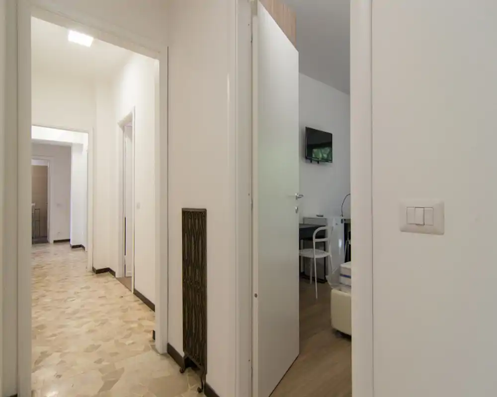 Ingresso/corridoio luminoso con pavimento in marmette e vista sulle stanze adiacenti, con una porta parzialmente aperta che mostra un piccolo locale arredato.