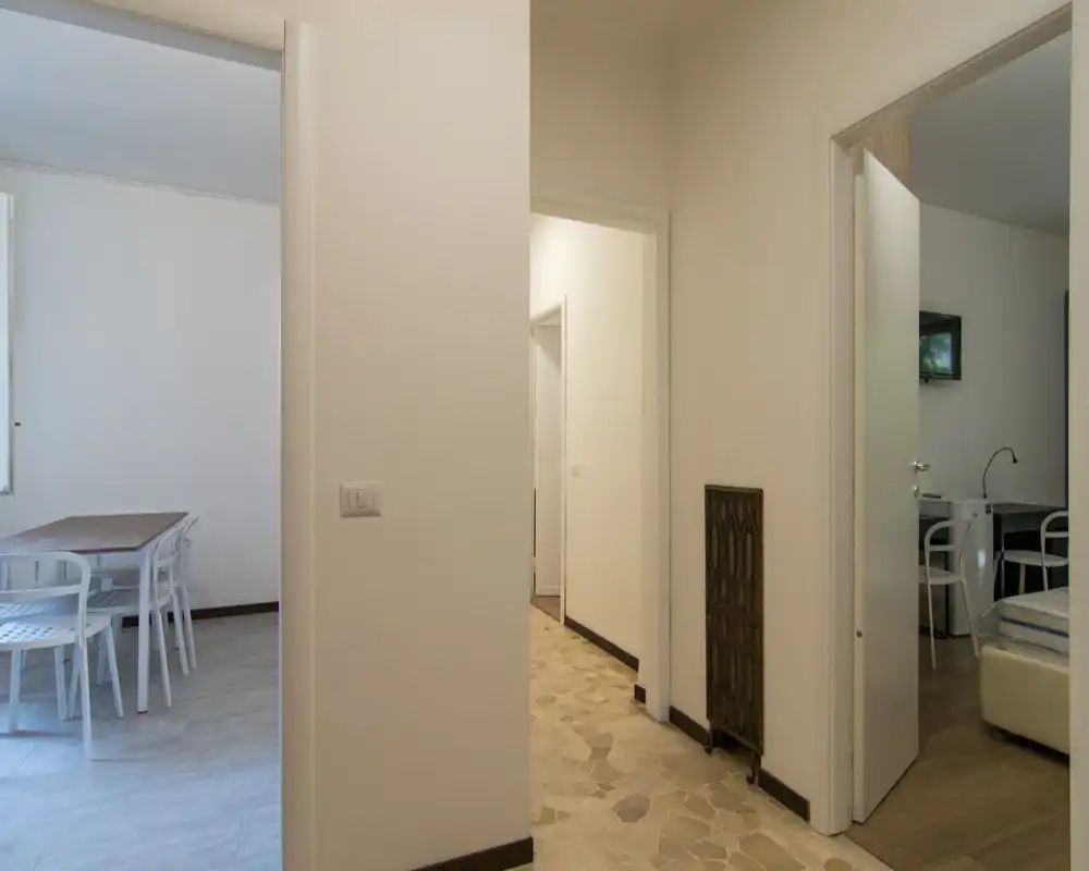 Ingresso luminoso e semplice con pavimento piastrellato che conduce alle stanze adiacenti; pareti neutre e visuale verso la zona pranzo e una piccola camera/ufficio.