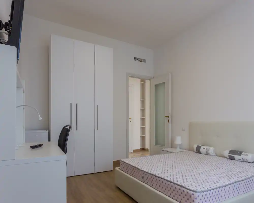 Dormitorio moderno y luminoso con cama doble, mesita y armario; tonos neutros y decoración minimalista que crean un espacio tranquilo y ordenado perfecto para un anuncio.
