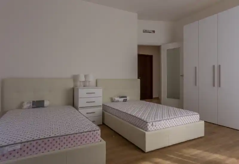 Dormitorio luminoso y minimalista con dos camas individuales, una mesita central y un gran armario. Las líneas limpias y los tonos neutros crean un ambiente moderno y tranquilo, perfecto para alquileres.