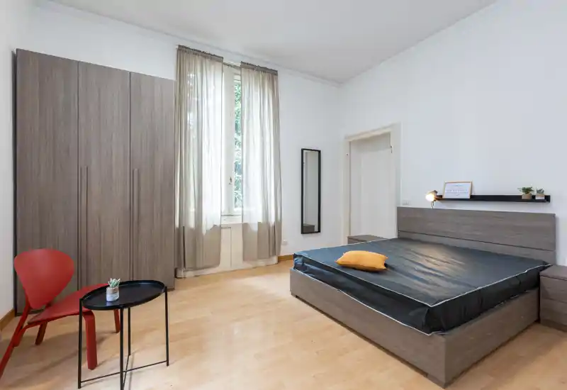 Dormitorio moderno y luminoso con cama grande, muebles en tono madera coordinados y una ventana alta que llena la habitación de luz natural.