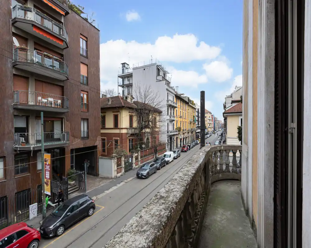 Balcone cittadino soleggiato con ringhiera in pietra che si affaccia su una tranquilla via residenziale e palazzi classici — ideale per un caffè mattutino o un piccolo angolo relax.